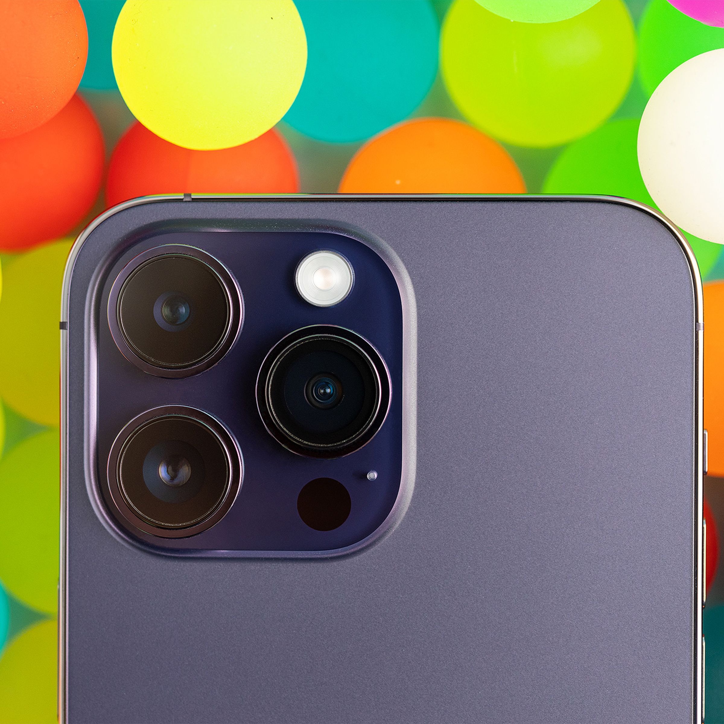 A close-up of the iPhone 14 Pro's camera module against a background of translucent colorful balls.